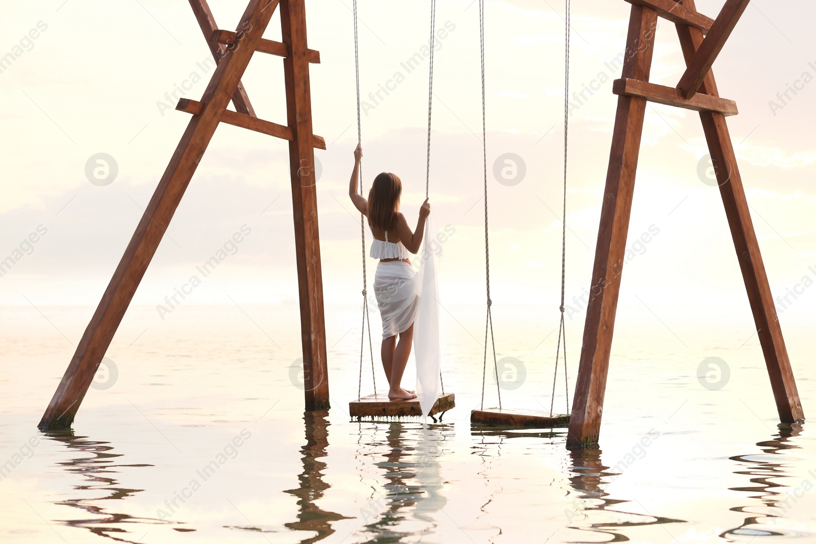 Photo of Young woman enjoying sunrise on swing over water