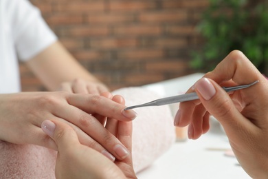Photo of Manicurist removing cuticle from client's nails with pusher at table, closeup. Spa treatment