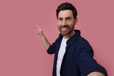 Photo of Smiling man taking selfie on pink background, space for text