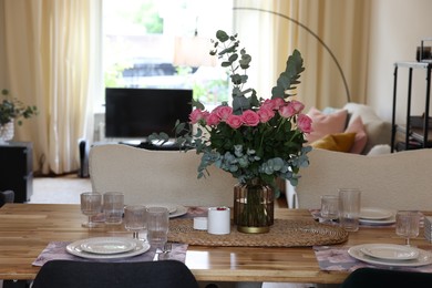 Beautiful table setting with bouquet of roses, napkins and candles in room