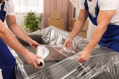 Photo of Workers wrapping sofa in stretch film indoors, closeup