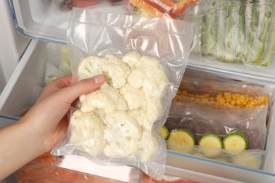 Photo of Woman putting vacuum bag with cauliflowers into fridge, closeup. Food storage