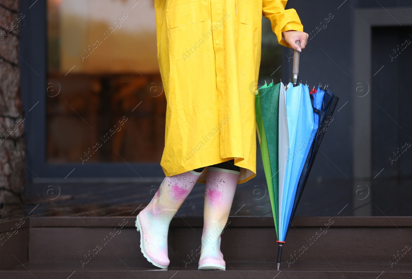 Image of Woman wearing raincoat and rubber boots holding umbrella outdoors, closeup