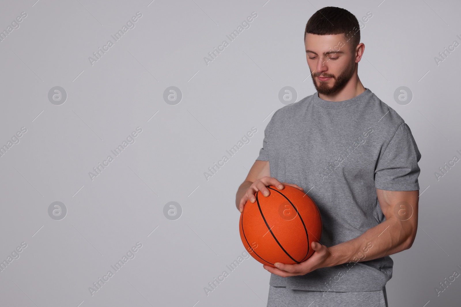 Photo of Athletic young man with basketball ball on light grey background. Space for text