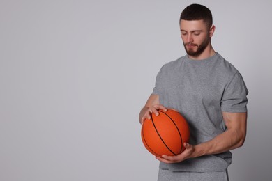 Photo of Athletic young man with basketball ball on light grey background. Space for text