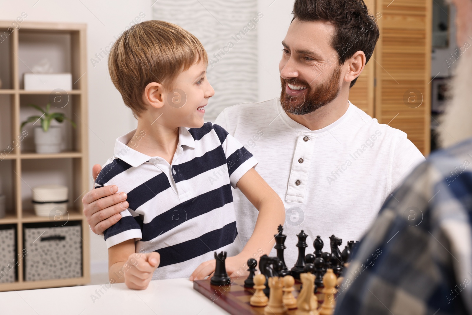 Photo of Family playing chess together at table in room