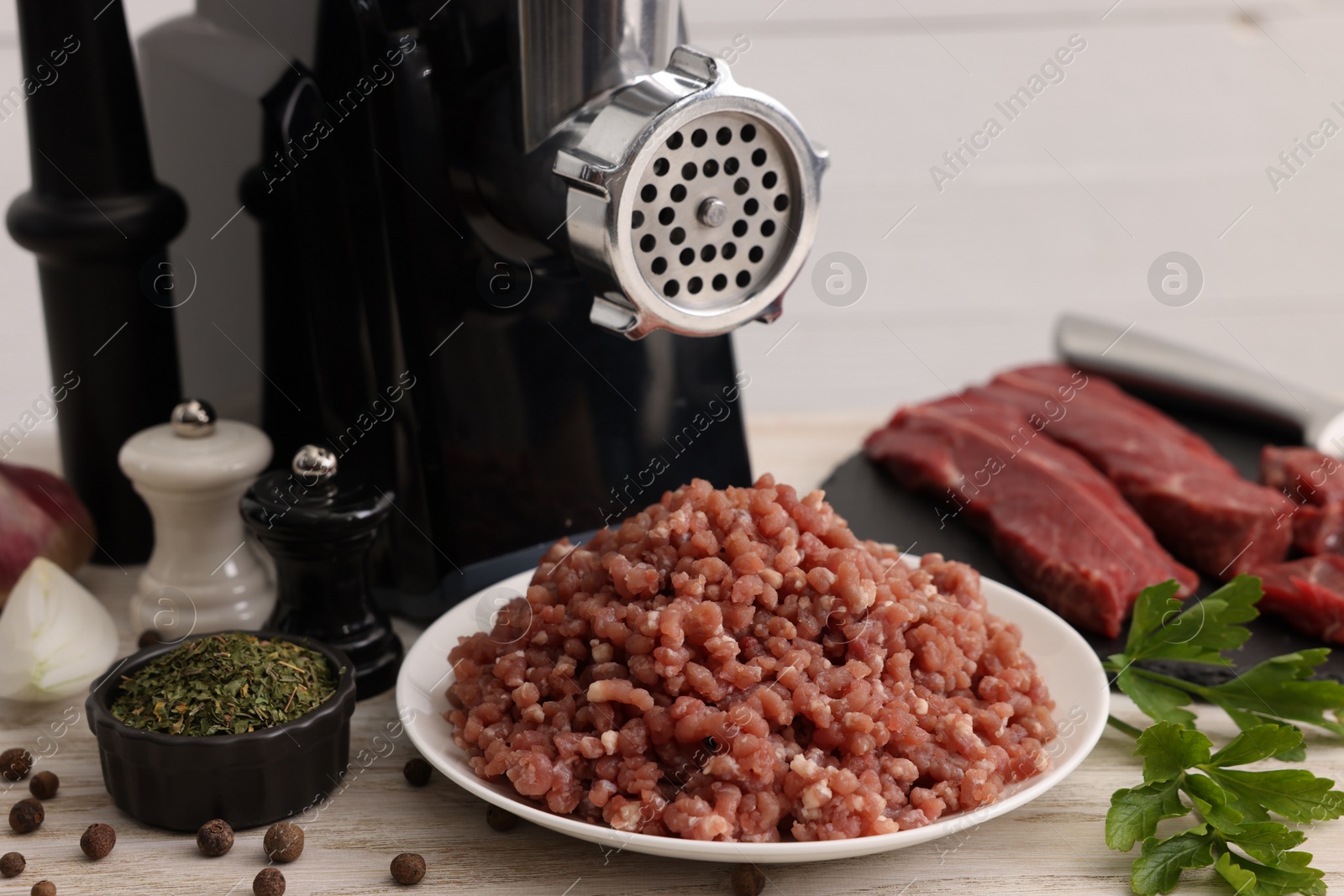 Photo of Electric meat grinder with beef, spices and parsley on white wooden table