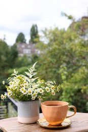 Photo of Cup of delicious chamomile tea and fresh flowers outdoors