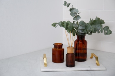 Eucalyptus branches, aromatic reed air freshener and candle on white table, space for text. Interior element