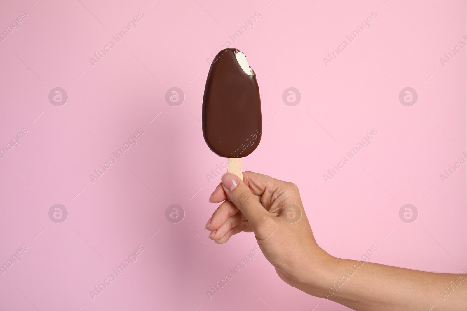 Photo of Woman holding bitten ice cream glazed in chocolate on pink background, closeup