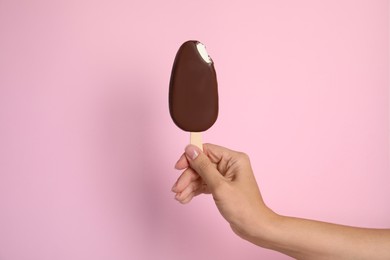 Photo of Woman holding bitten ice cream glazed in chocolate on pink background, closeup