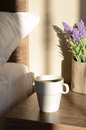 Cup of coffee on wooden night stand near bed in morning