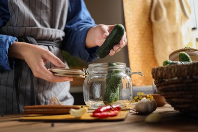 Photo of Woman putting cucumbers into jar at wooden table, closeup. Pickling vegetables