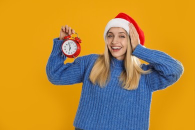 Photo of Woman in Santa hat with alarm clock on yellow background. New Year countdown