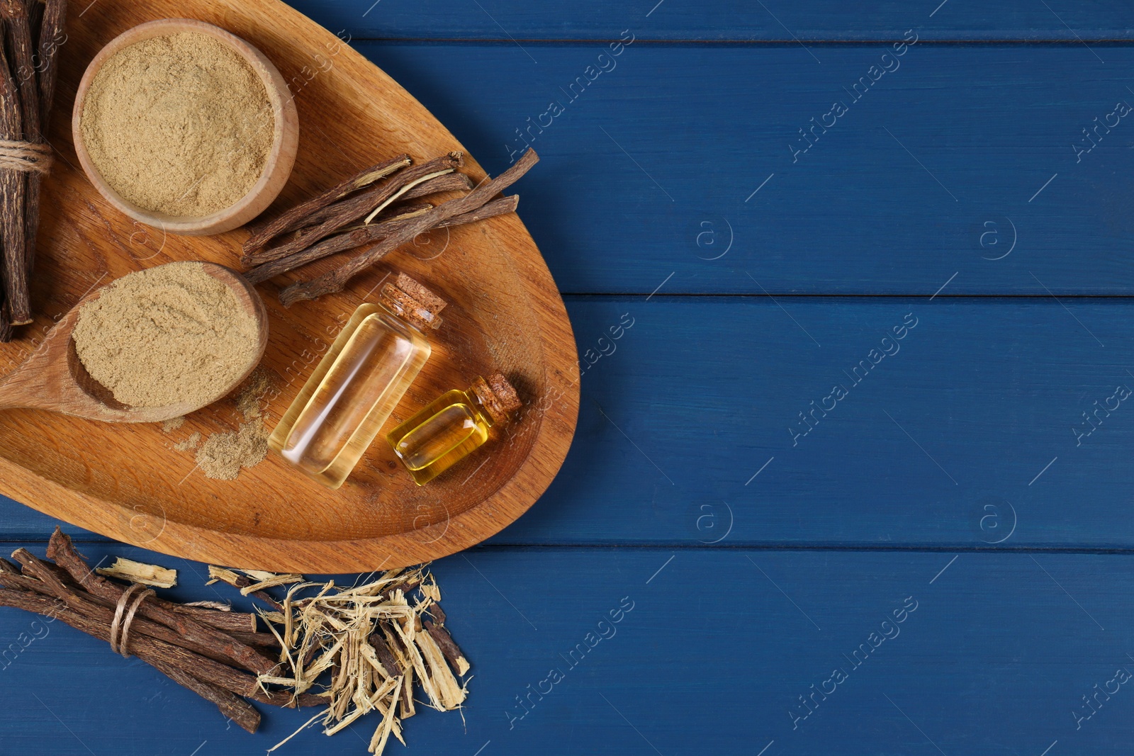 Photo of Dried sticks of licorice root, powder and essential oil on blue wooden table, flat lay. Space for text
