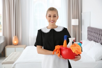 Photo of Young chambermaid with cleaning supplies in bedroom