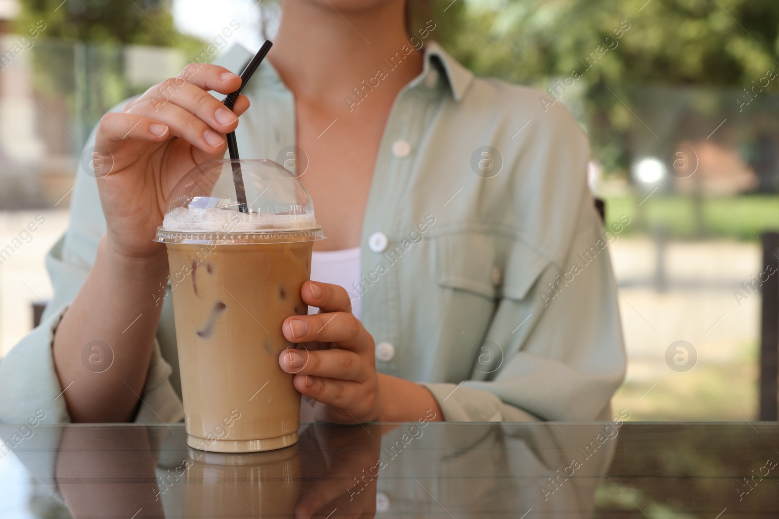 Photo of Woman with plastic takeaway cup of delicious iced coffee at table in outdoor cafe, closeup. Space for text