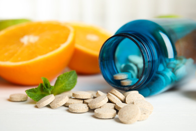 Photo of Bottle with vitamin pills and orange on white wooden table, closeup