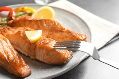 Tasty cooked salmon with lemon on plate, closeup