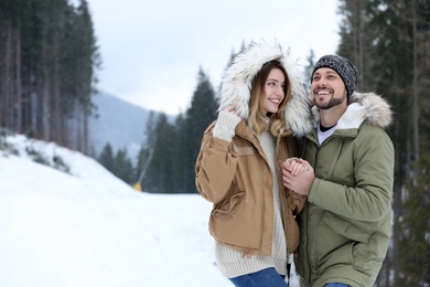 Photo of Happy couple near conifer forest on snowy day, space for text. Winter vacation