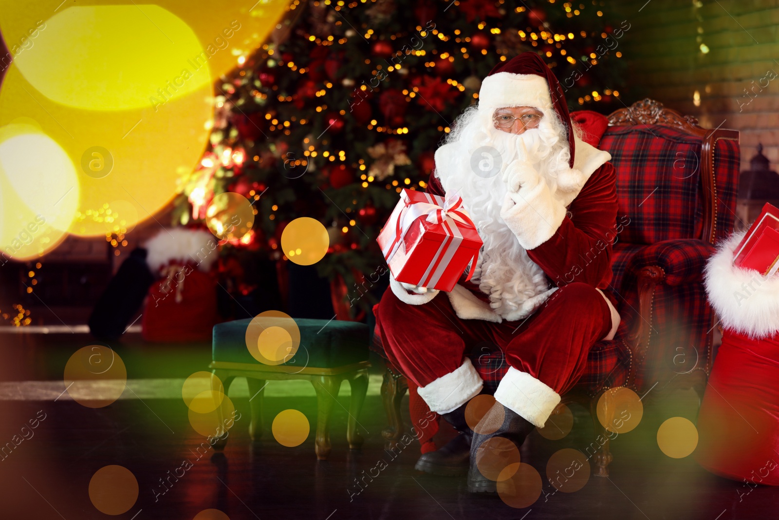 Photo of Santa Claus with gift box near Christmas tree indoors