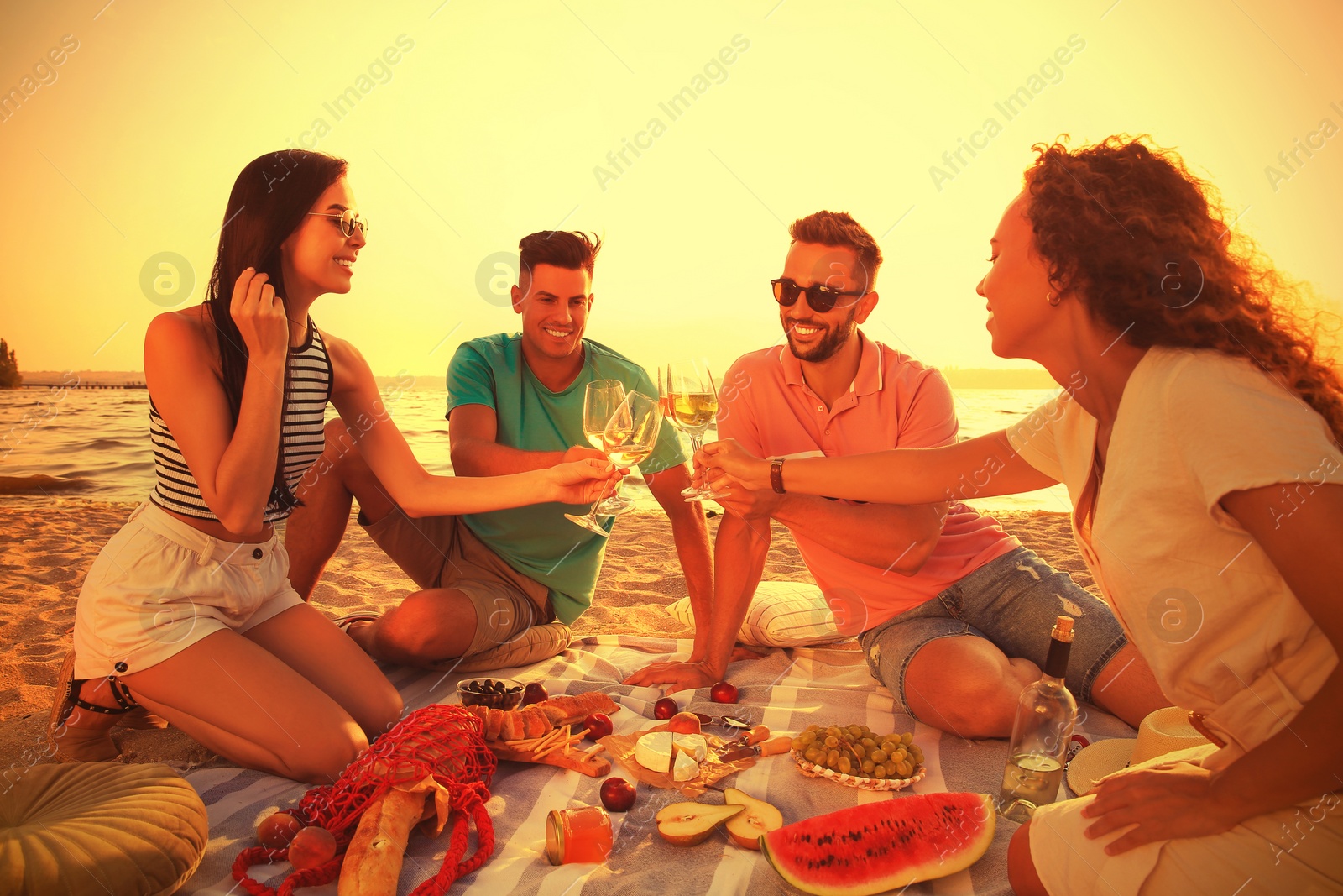 Image of Group of friends having picnic outdoors at sunset