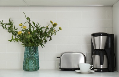 Photo of Modern toaster, coffeemaker and beautiful bouquet on countertop in kitchen