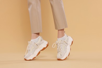 Woman wearing pair of new stylish sneakers on beige background, closeup