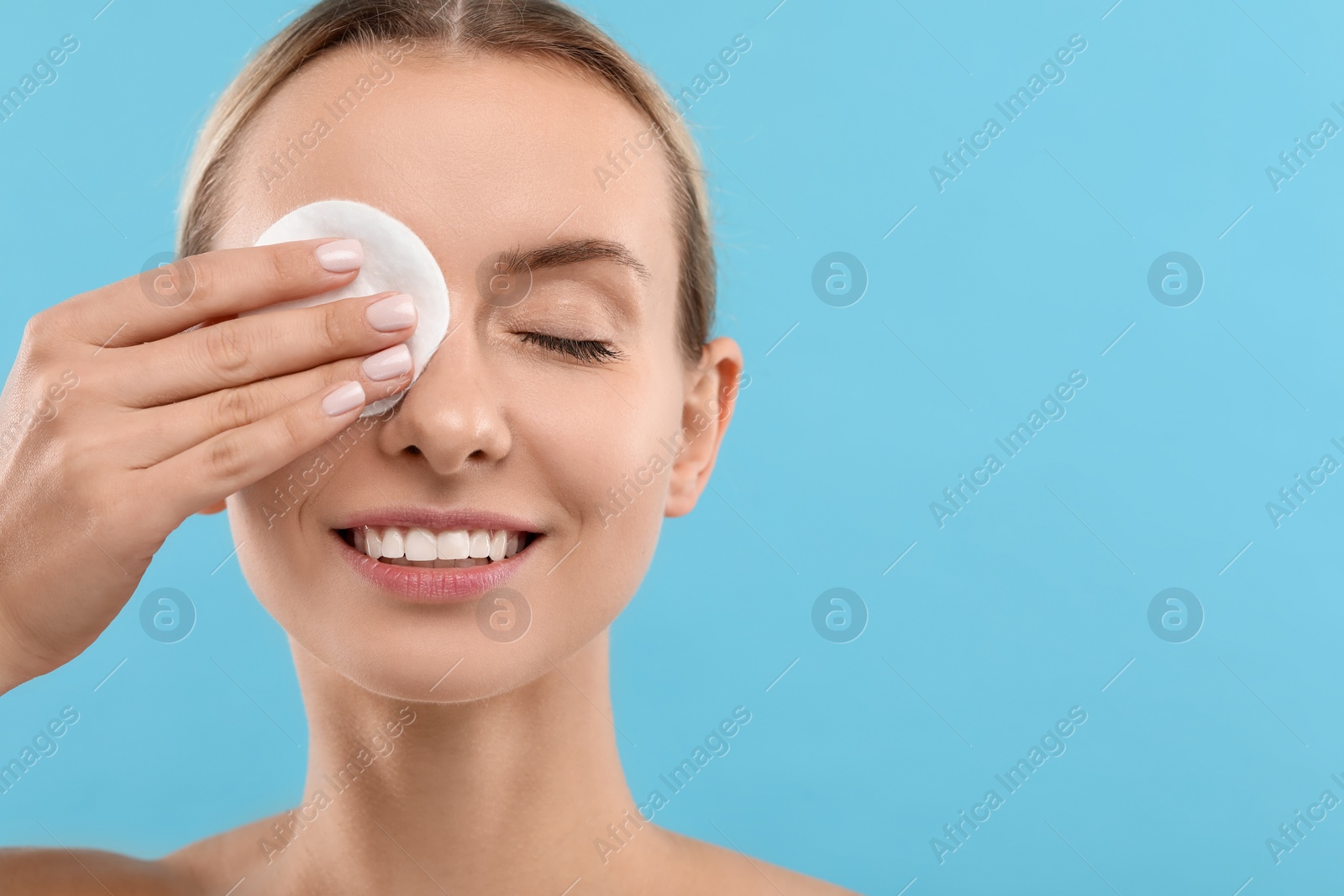 Photo of Smiling woman removing makeup with cotton pad on light blue background, closeup. Space for text