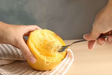 Photo of Woman scraping flesh of cooked spaghetti squash with fork on table