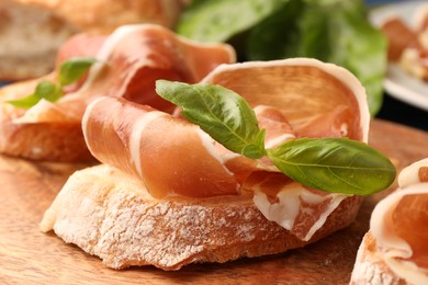 Photo of Tasty sandwiches with cured ham and basil leaves on wooden board, closeup