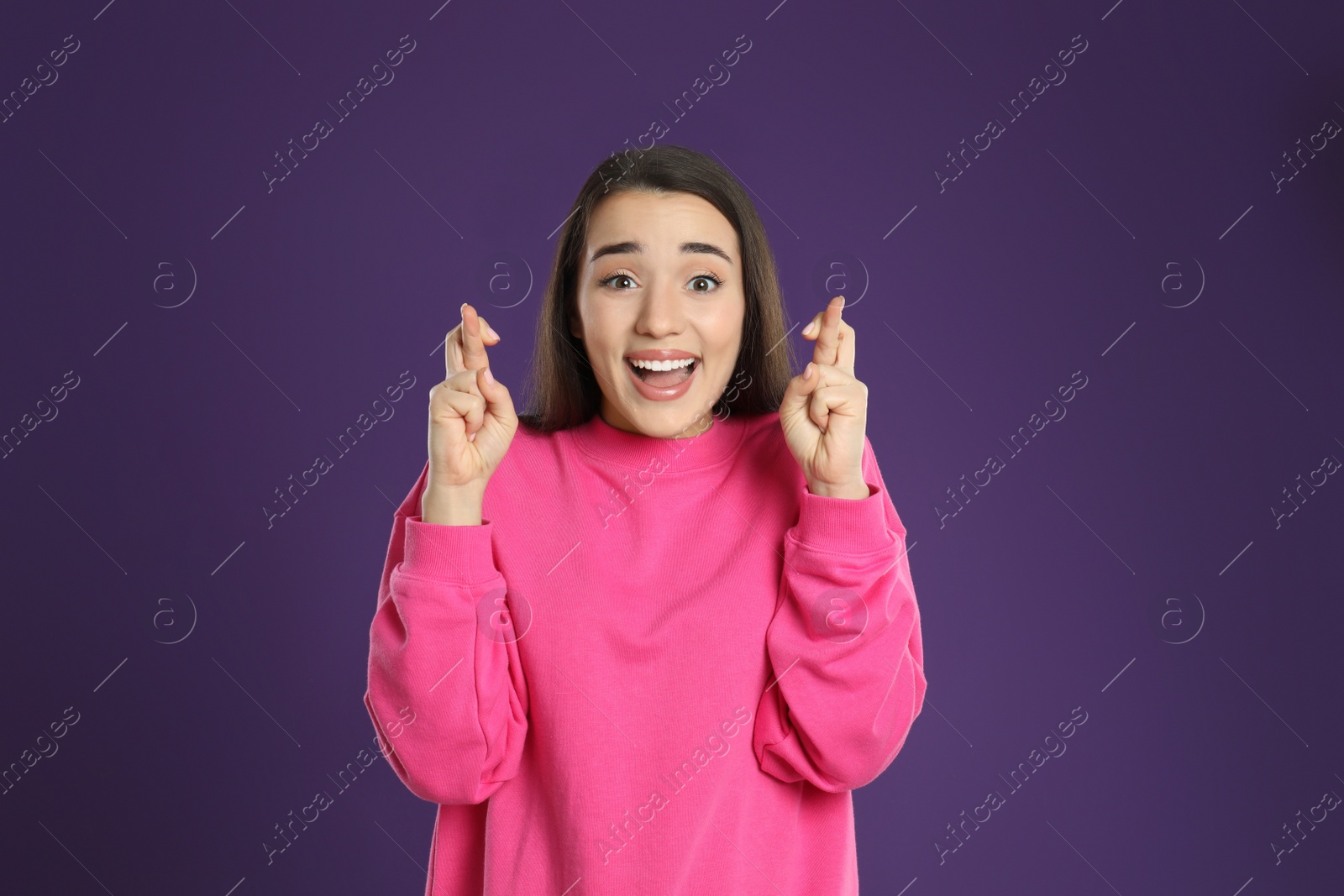 Photo of Woman with crossed fingers on purple background. Superstition concept