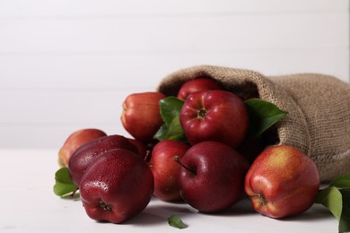 Photo of Ripe red apples and green leaves on white table