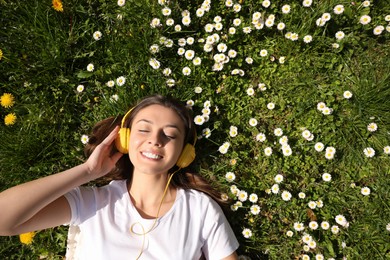 Photo of Happy woman listening to audiobook while lying on grass among blooming daisies, top view