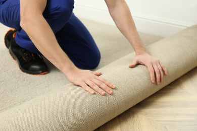 Photo of Worker rolling out new carpet flooring indoors, closeup