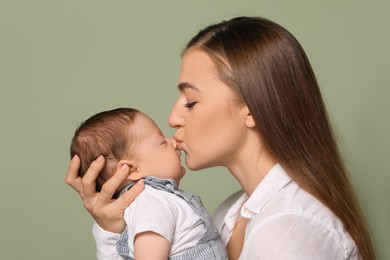 Photo of Mother kissing her cute newborn baby on olive background