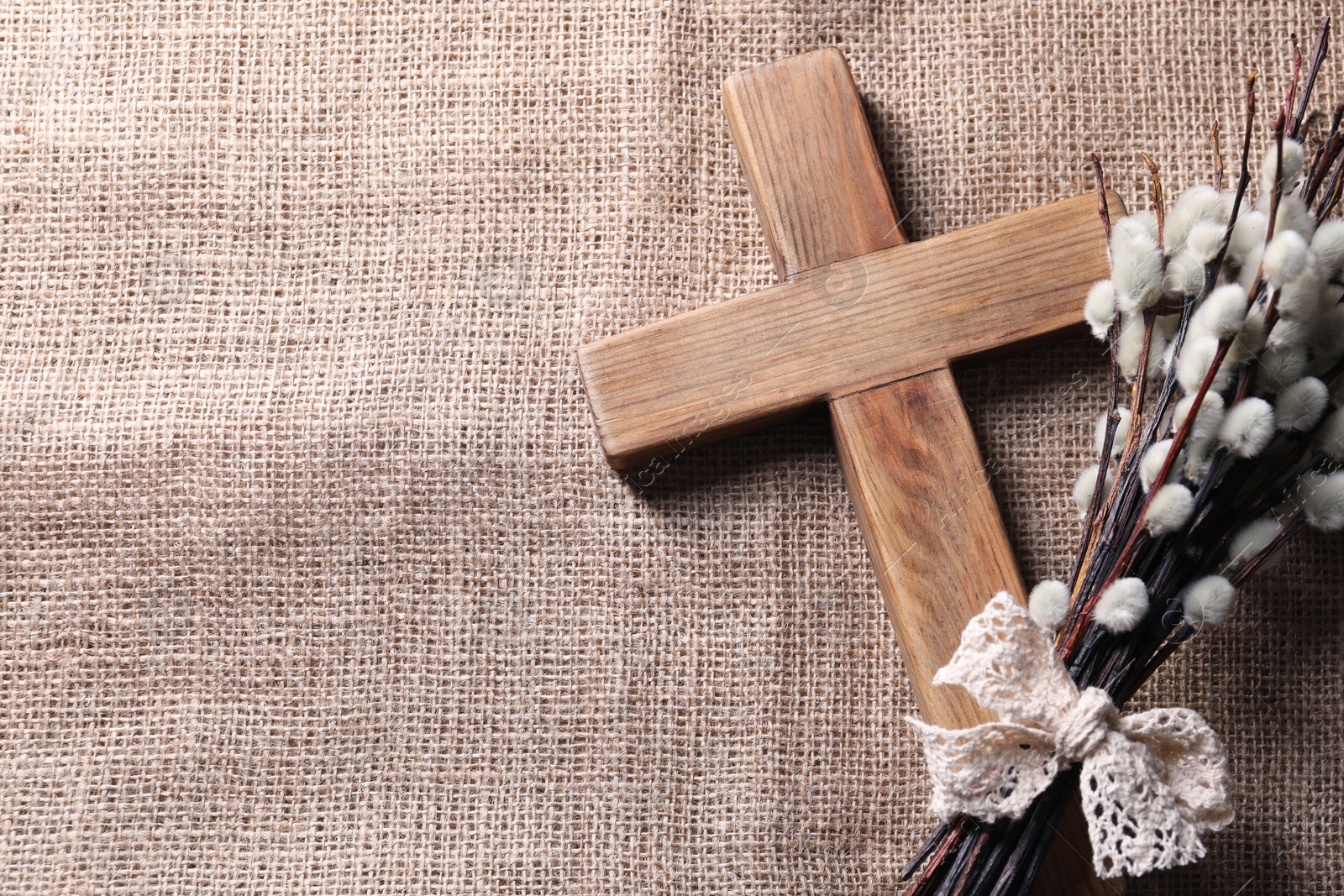 Photo of Cross and willow branches on beige cloth, flat lay. Space for text