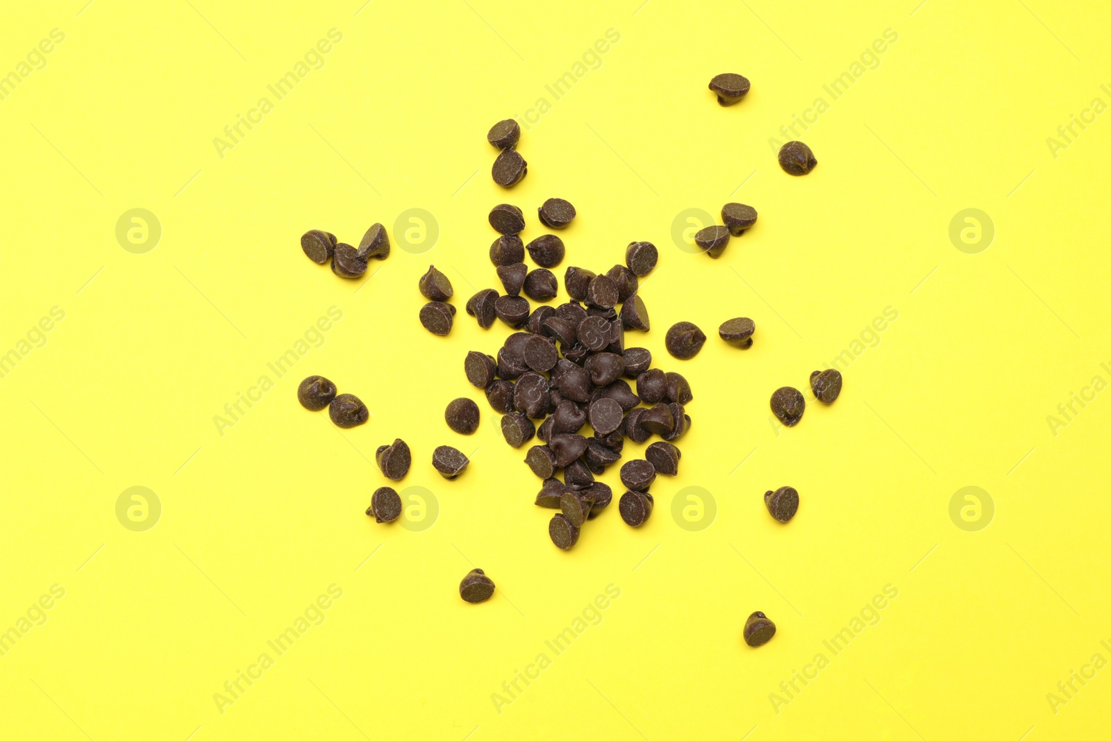 Photo of Pile of delicious chocolate chips on yellow background, top view