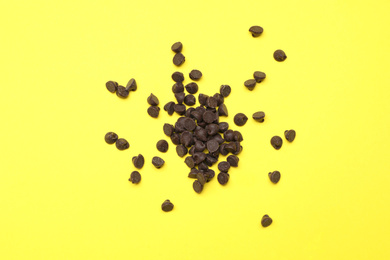 Photo of Pile of delicious chocolate chips on yellow background, top view