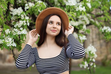 Beautiful woman in hat near blossoming tree on spring day