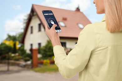 Woman using home security system application on smartphone outdoors, closeup