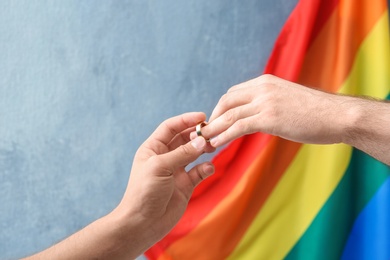 Young man putting wedding ring on his boyfriend's finger near rainbow flag. Gay marriage