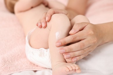 Photo of Woman applying body cream onto baby`s skin on bed, closeup