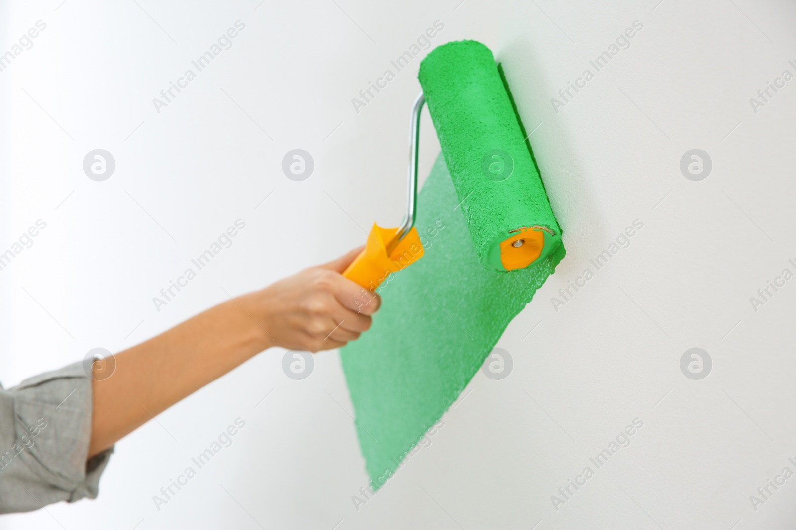 Photo of Woman painting white wall with green dye, closeup. Interior renovation