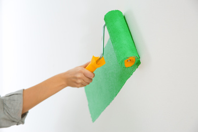 Photo of Woman painting white wall with green dye, closeup. Interior renovation