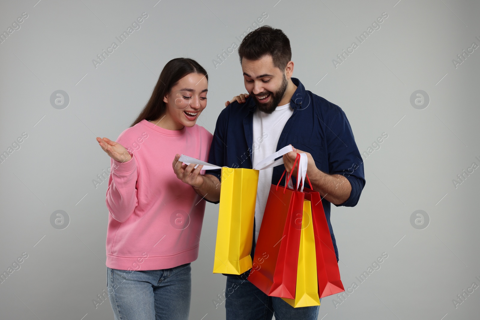 Photo of Man showing to his girlfriend shopping bag with purchase on grey background