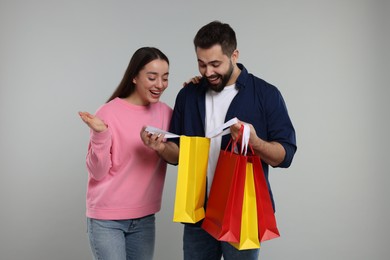 Man showing to his girlfriend shopping bag with purchase on grey background