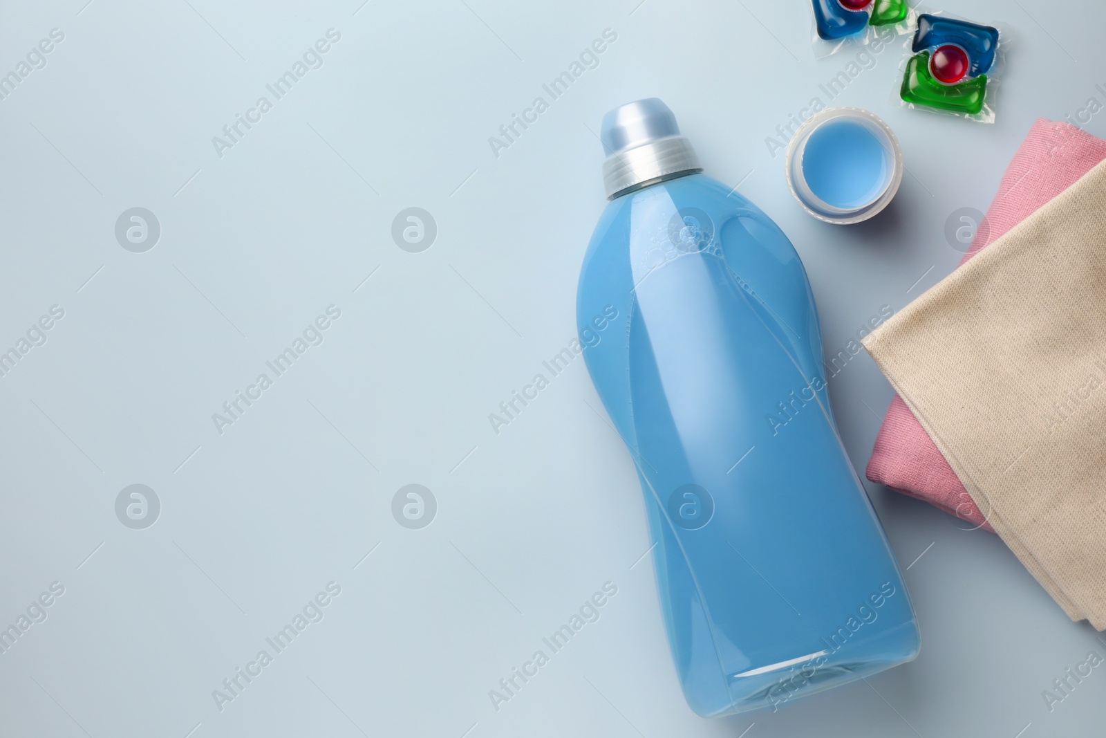 Bottle of fabric softener, laundry capsules and stacked clean clothes on light background, flat lay. Space for text Photo of Bottle of fabric softener, laundry capsules and stacked clean clothes on light background, flat lay. Space for text