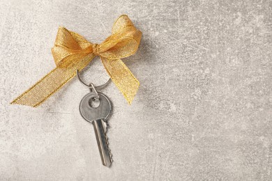 Photo of Key with golden bow on light grey stone background, top view and space for text. Housewarming party