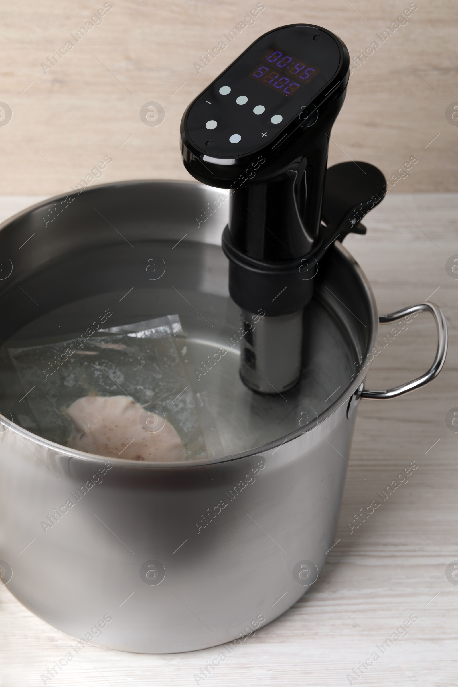 Photo of Thermal immersion circulator and vacuum packed meat in pot on white wooden table. Sous vide cooking